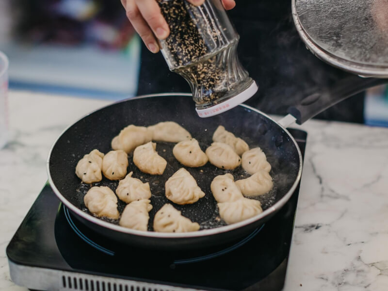 Person using a metal spatula to flip a pan full of gyoza dumplings